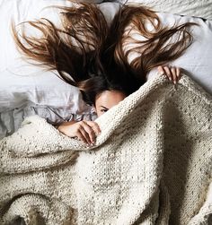 a woman laying in bed under a blanket with her hair flying above her head as she covers herself from the sun