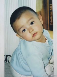 a baby is sitting on the floor and looking at the camera while wearing a blue shirt