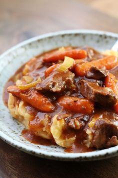 a white bowl filled with meat and carrots on top of a wooden table next to a fork