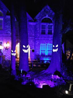 purple halloween lights in front of a house with scary faces on the trees and bushes