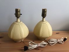 two yellow lamps sitting on top of a wooden table next to wires and plugs