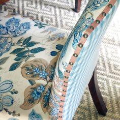 the back of a chair with blue and white flowers on it, sitting in front of a patterned rug