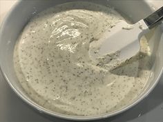 a bowl filled with white sauce and a spatula in it's center, on top of a table