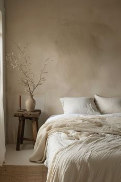 a white bed sitting next to a wooden table with a vase on top of it