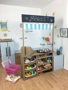 a child's play area with toys and other items on the floor in front of a market sign