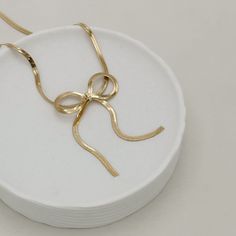 We all know how bows are having a serious moment right now, and we couldn't resist incorporating this trend into our latest Summer Collection right now. The Riley Bow Necklace is both sophisticated and playful, the perfect amount of glamour to wear around your neck.. Meticulously crafted from quality 18k gold filled, this piece features a refined 3mm Herringbone Snake Ribbon Bowtie that brings out the little girl in all of us. At 16 inches in length, it's the perfect everyday accessory to seamle Chic Yellow Gold Necklaces For Evening, Elegant Gold Necklace With Decorative Bow, Gold Bow Necklace For Party, Gold Necklace With Bow For Party, Elegant Gold Necklace With Bow Detail, Elegant Gold Necklace With Bow, Chic Jewelry With Butterfly Knot For Parties, Gold Necklace With Ribbon For Gift, Gold Necklace With Ribbon Perfect For Gifts