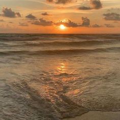 the sun is setting over the ocean with waves crashing in front of it and some clouds