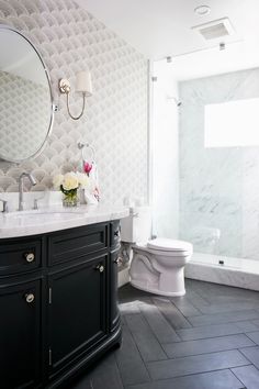 a white toilet sitting next to a black cabinet in a bathroom under a large mirror