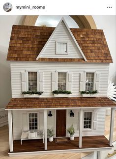 a white doll house with brown roof and windows on top of a wooden floor in front of a window