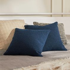 three blue pillows on a bed in a room with white headboard and beige walls