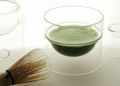 a whisk in a glass next to three glasses filled with green colored liquid