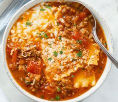 a white bowl filled with pasta and meat soup on top of a marble countertop