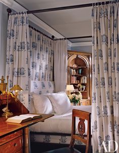 a bed sitting next to a desk with a lamp on top of it in front of a window