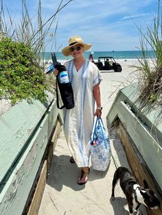 a woman with two bags and a dog on the beach