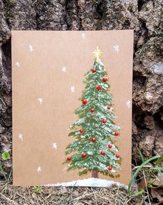 a card with a christmas tree on it sitting in front of a tree trunk and snowflakes