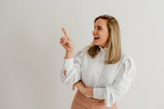 a woman in a white shirt and tan skirt pointing to the side with her finger