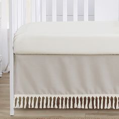 a white crib with a beige bed skirt on it's bottom and side