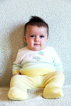 a baby is sitting on the couch and looking at the camera