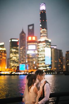 the bride and groom are standing by the water in front of the cityscape