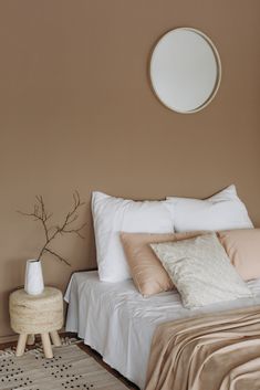 a bed with white sheets and pillows in a bedroom next to a round mirror on the wall