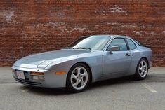 a silver sports car parked in front of a brick wall