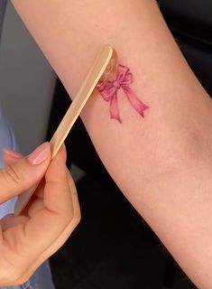 a woman with a pink bow tattoo on her arm holding a wooden comb in her left hand