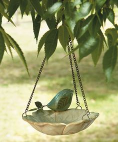 a green bird sitting on top of a bowl hanging from a tree