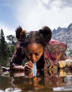 a woman bending over to look at something in the water with mountains in the background