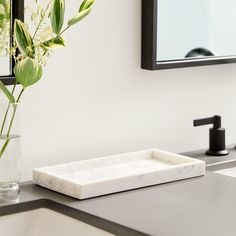 a vase with some flowers in it sitting on a counter next to a sink and mirror