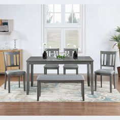 a dining room table with chairs and a bench in front of a window on a rug