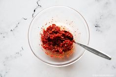 a glass bowl filled with red stuff on top of a white counter next to a spoon