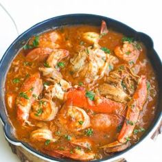 a pot filled with meat and vegetables on top of a white table cloth next to a spoon