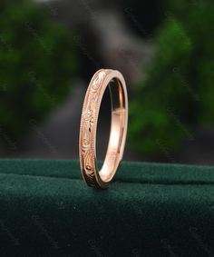 a gold wedding band with engraved design on the inside and outside, sitting on a green velvet surface