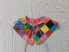 a multicolored bib laying on top of a white sheet with string attached to it