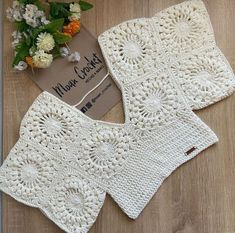 two white crocheted dishcloths on a wooden table next to a bouquet of flowers