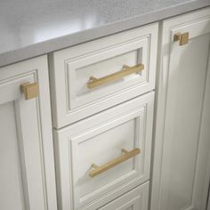 a kitchen with white cabinets and marble counter tops, gold pulls on the drawer handles