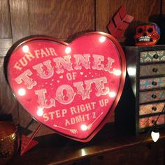 a heart shaped neon sign sitting on top of a wooden table next to a dresser