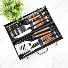 an assortment of kitchen utensils in a black box next to a potted plant