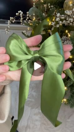 a person holding a green bow in front of a christmas tree