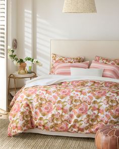 a bed with pink flowers on it in a bedroom next to a table and lamp