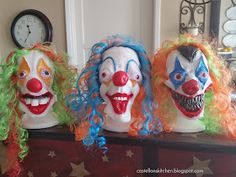 three creepy clown masks sitting on top of a table next to a clock and other decorations