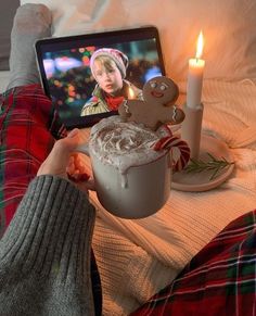 a person sitting on a bed next to a laptop with a gingerbread drink in front of them