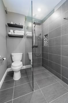 a bathroom with gray tiles and white fixtures, including a toilet and walk in shower