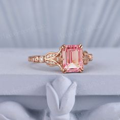 a pink tourmaline and diamond ring sitting on top of a white cloth covered box