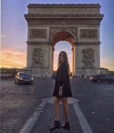 a woman is standing in front of the arc de triomphe at sunset with her hand on her hip