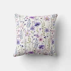 a white pillow with purple flowers and leaves on the front, sitting against a wall