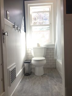 a white toilet sitting next to a window in a bathroom on top of a hard wood floor