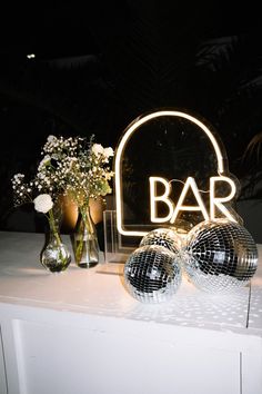 a bar sign with disco balls and vases sitting on a white countertop in front of it