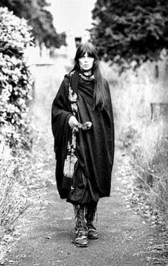 black and white photograph of a woman walking down a path wearing a long cape with flowers on it