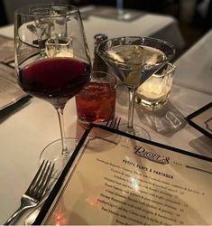 two glasses of wine sit on a table next to an empty menu and utensils